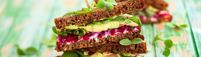 Skuteczne sposoby na zaparcia - dieta bogata w błonnik i leki homeopatyczne. Kanapki z ciemnego pieczywa z burakami, awokado i sałatą na rustykalnym zielonym drewnianym blacie.