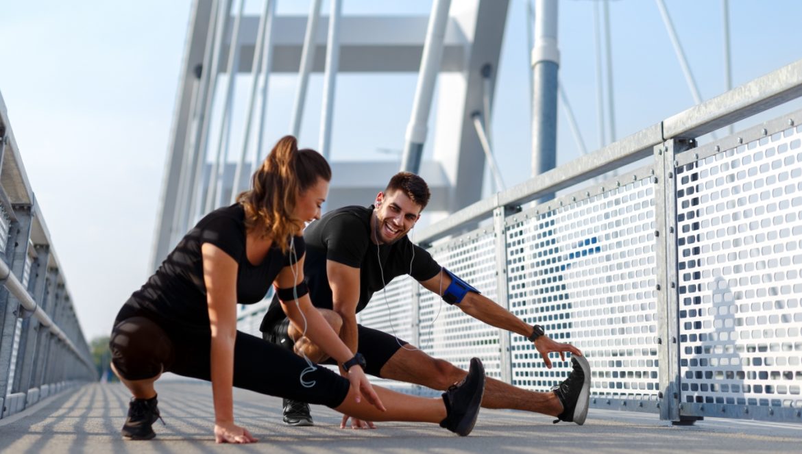 Sport jest dla wszystkich - jakie są korzyści ze sportu amatorskiego, a jakie zagrożenia niesie sport wyczynowy? Kobieta i mężczyzna rozciągają się po treningu w mieście.
