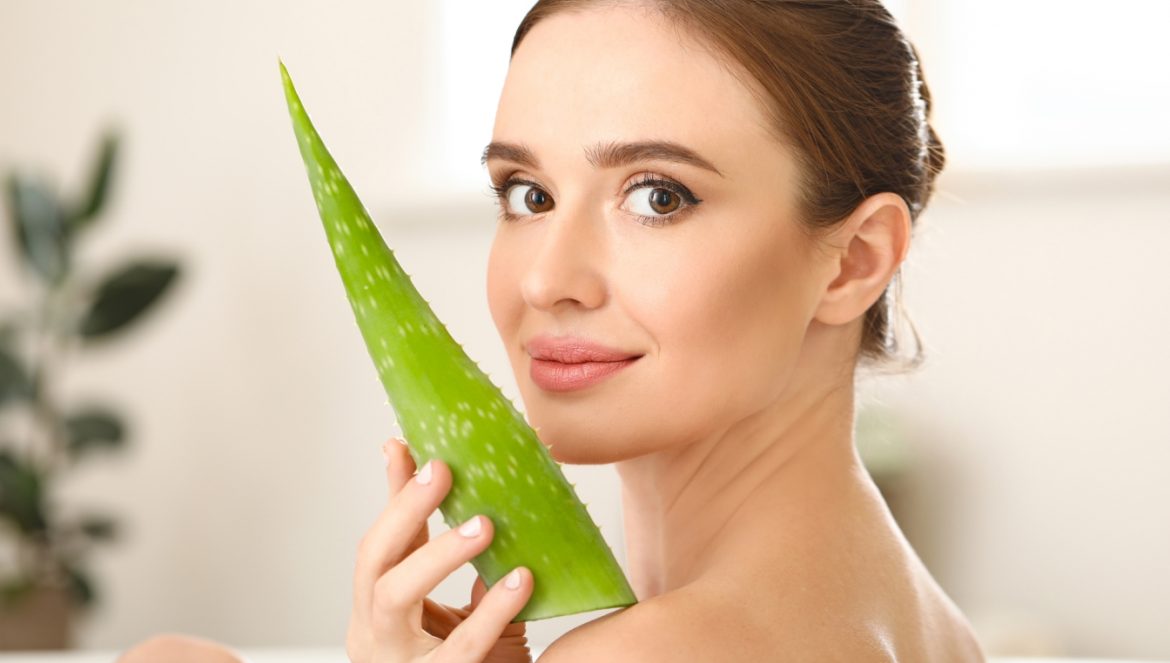 Aloes na twarz, włosy i skórę. Jak wykorzystać lecznicze właściwości aloesu w kosmetyce? Piękna kobieta trzyma przy twarzy liść aloesu.