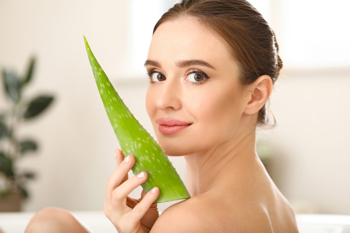 Aloes na twarz, włosy i skórę. Jak wykorzystać lecznicze właściwości aloesu w kosmetyce? Piękna kobieta trzyma przy twarzy liść aloesu.