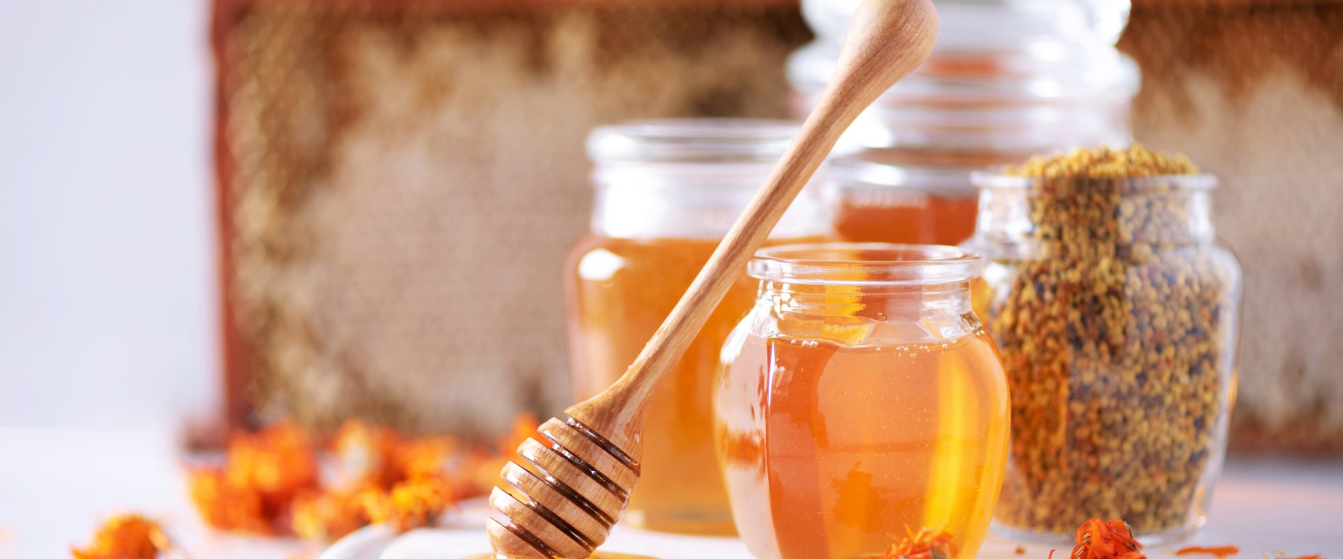 Apiterapia - leczenie produktami pszczelimi. Na czym polega? Miód i produkty pszczele na białej desce w kuchni.