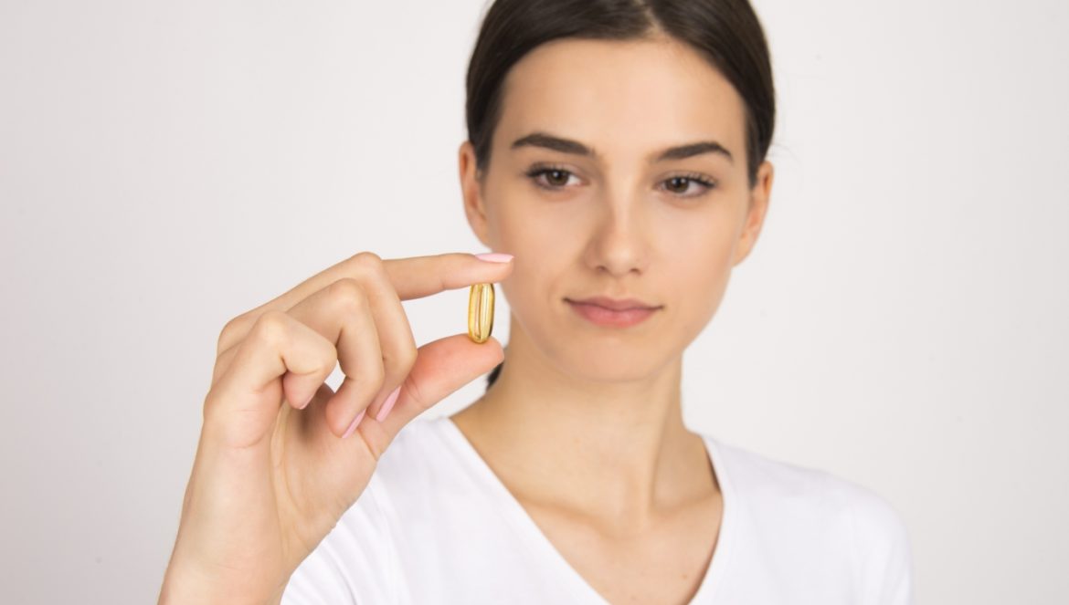 Suplementy z argininą - kiedy warto po nie sięgnąć? Kobieta przygląda się kapsułce preparatu.