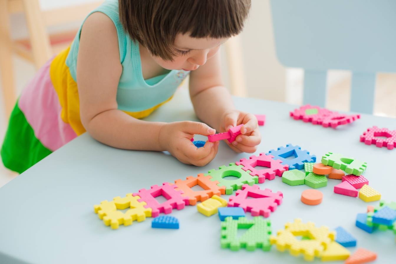 Dieta dla dzieci z autyzmem. Autystyczna dziewczynka układa kolorowe puzzle na stoliku w pokoju dziecięcym.