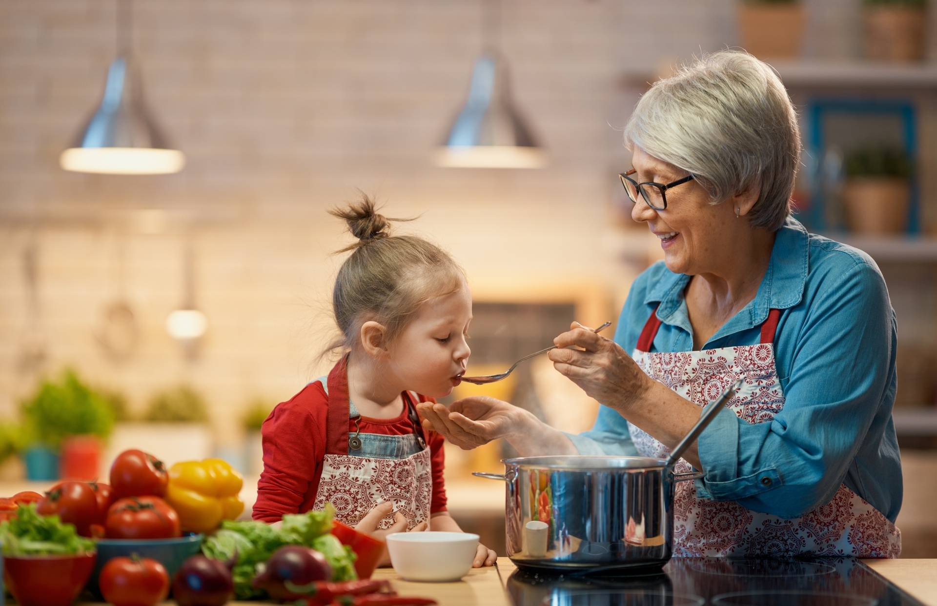 Wspólne posiłki i wspólne gotowanie z dzieckiem - dlaczego są takie ważne? Babcia uczy wnuczkę gotować w domowej kuchni.
