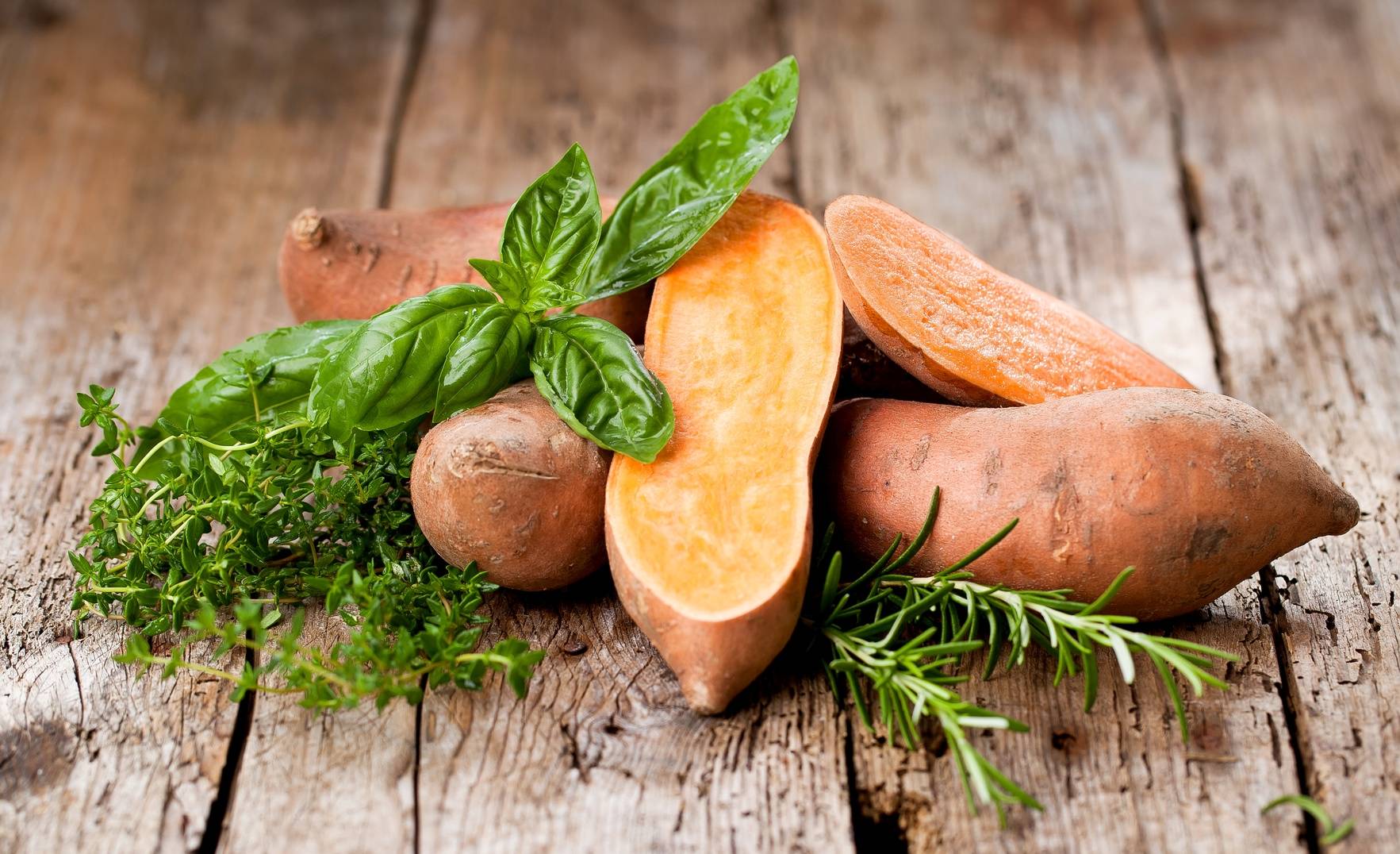 Bataty - słodkie ziemniaki ze świeżymi ziołami na drewnianym stole. Przepisy z batatów.