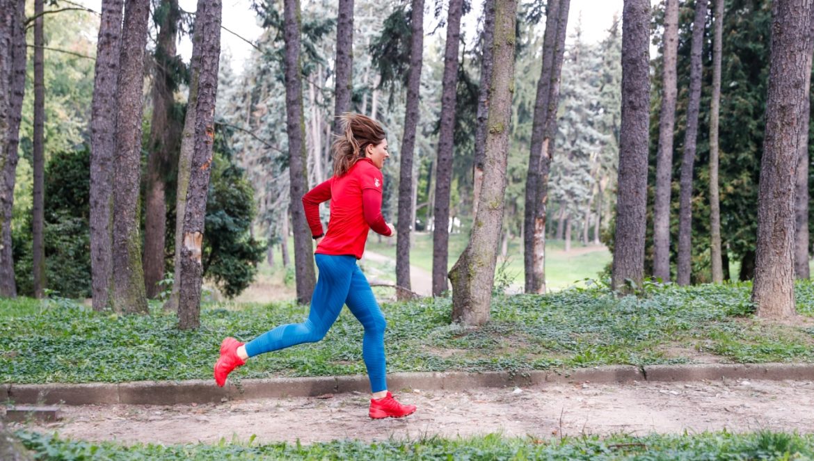 Bieganie dla początkujących. Jak zacząć biegać? Beata Sadowska w czerwonej bluzie i butach oraz niebieskich legginsach biega po parku.