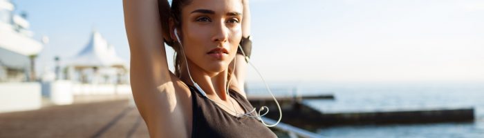 Jak zadbać o sprawną pracę powięzi? Rozciąganie i wysiłek fizyczny. Czym jest powięź? Młoda kobieta w czarnym topie sportowym rozciąga się po bieganiu na promenadzie nad morzem.