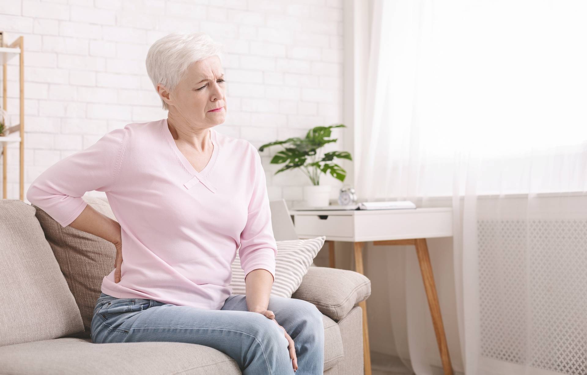Bóle krzyża - jaka jest przyczyna i jak im zaradzić? Starsza kobieta trzyma się za kręgosłup lędźwiowy.