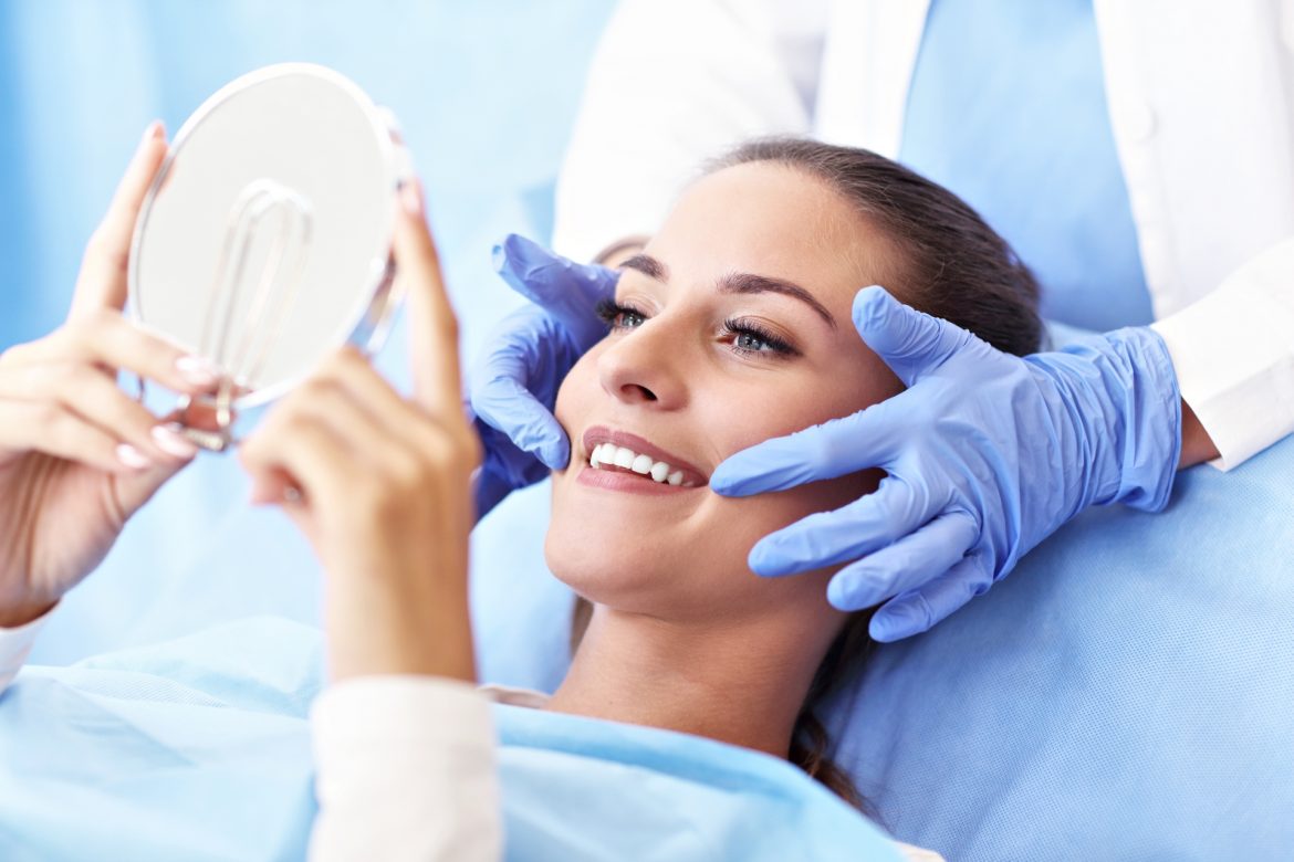 Bonding - prosty sposób na piękne zęby. Kobieta leżąca na fotelu dentystycznym patrzy w lusterko na swoje nowe białe zęby.