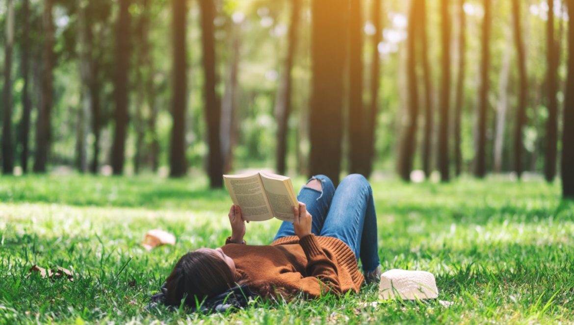 Borelioza - objawy, przyczyny, leczenie. Jak zdiagnozować boreliozę? Młoda kobieta czyta książkę na trawie w lesie.