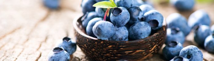 Jagody - jakie właściwości mają borówki leśne? Wysypujące się z koszyczka jagody na starym drewnianym stole.