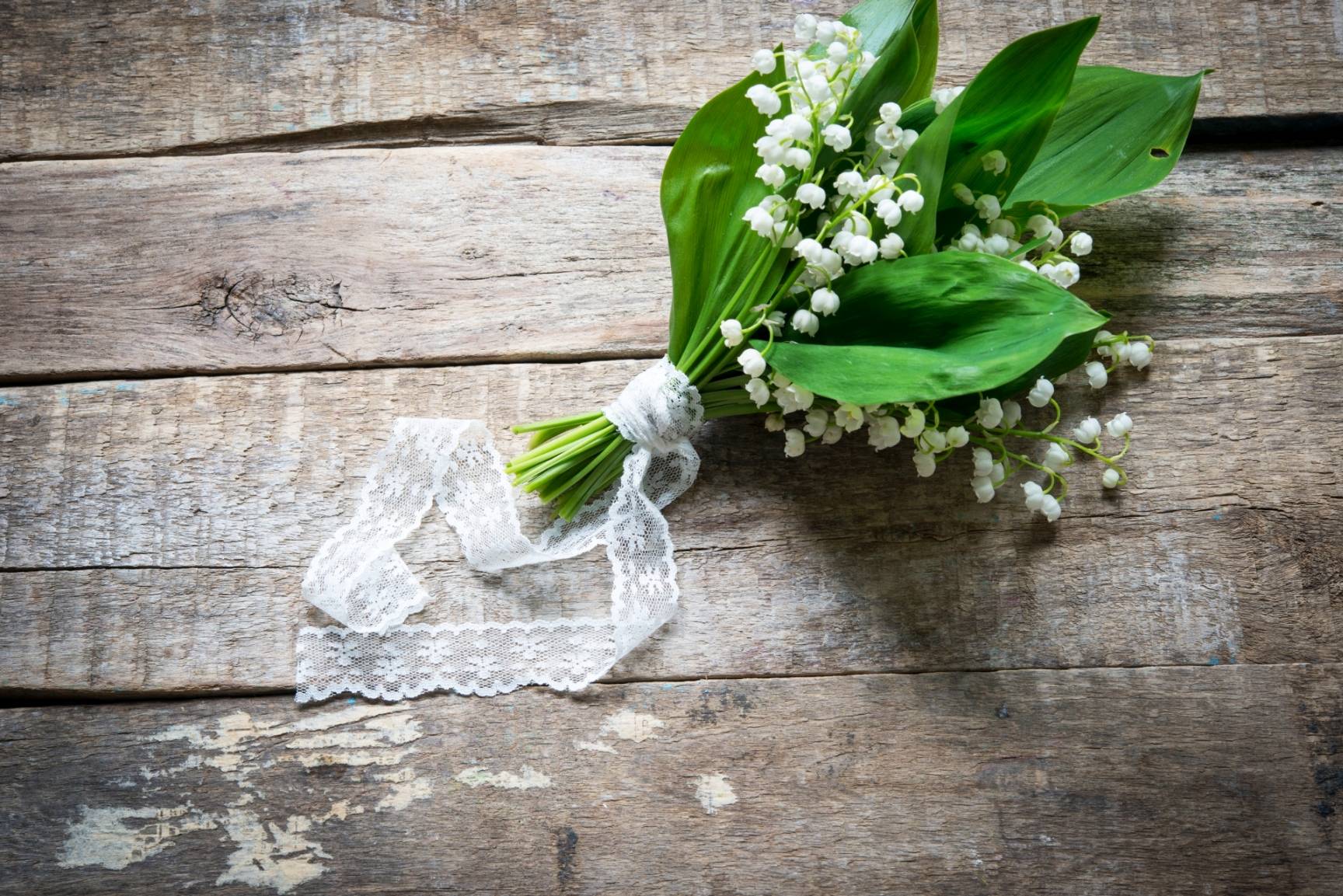 Konwalia majowa wspomaga pracę serca. Bukiecik konwalii obwiązany białą wstążką leży na starym drewnianym blacie.