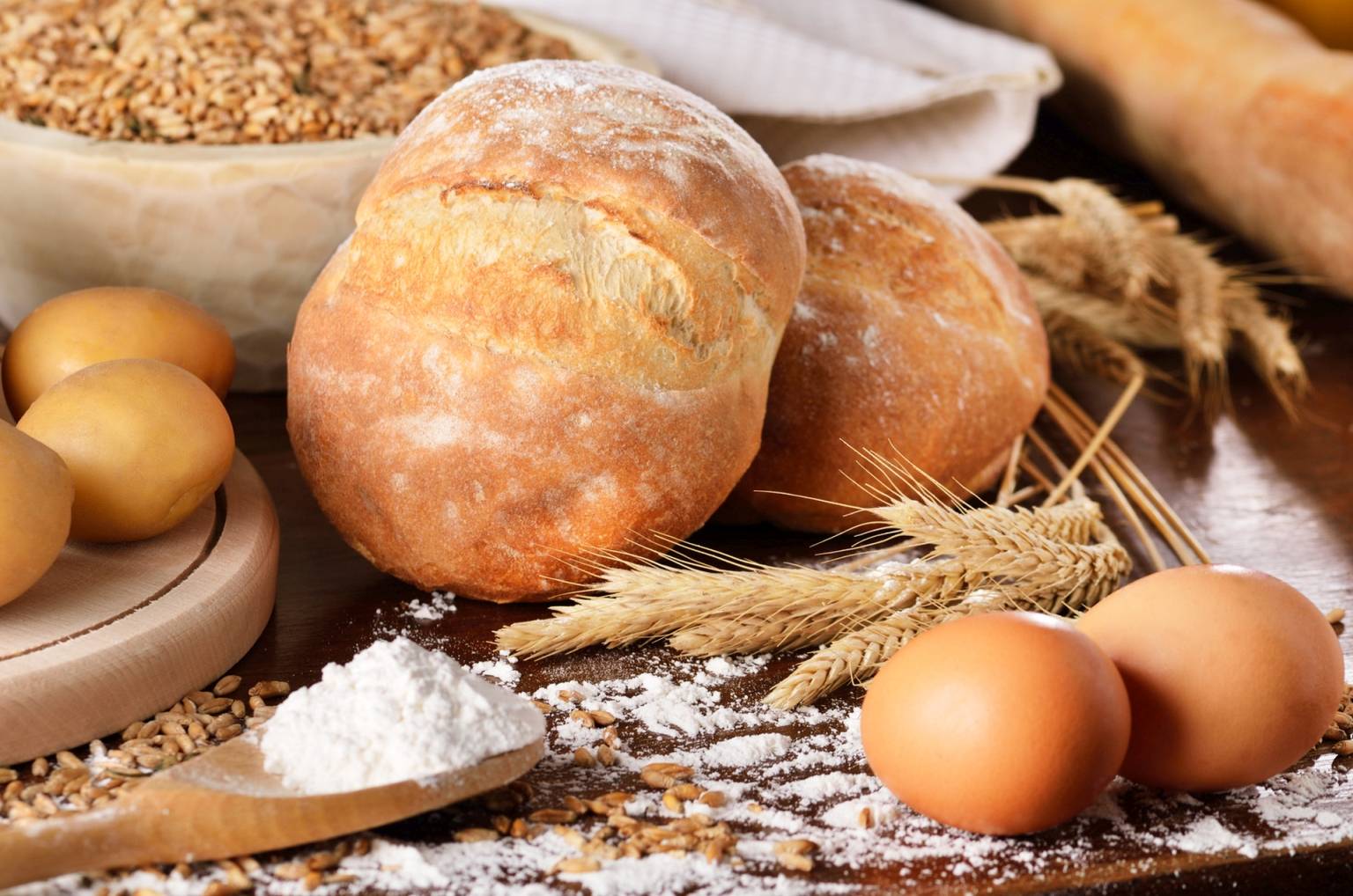 Celiakia - co to za choroba, jak się objawia i co ma wspólnego z dietą bezglutenową? Bułki pszenne, mąka pszenna i jajka na drewnianym stole.