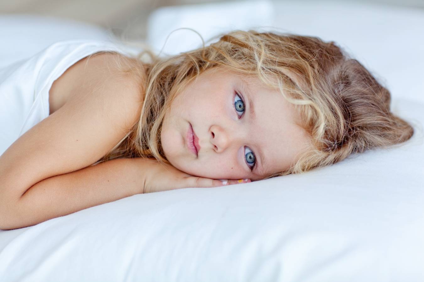 Jak leczyć zapalenie krtani u dzieci? Chora dziewczynka leży w łóżku ze smutną miną.
