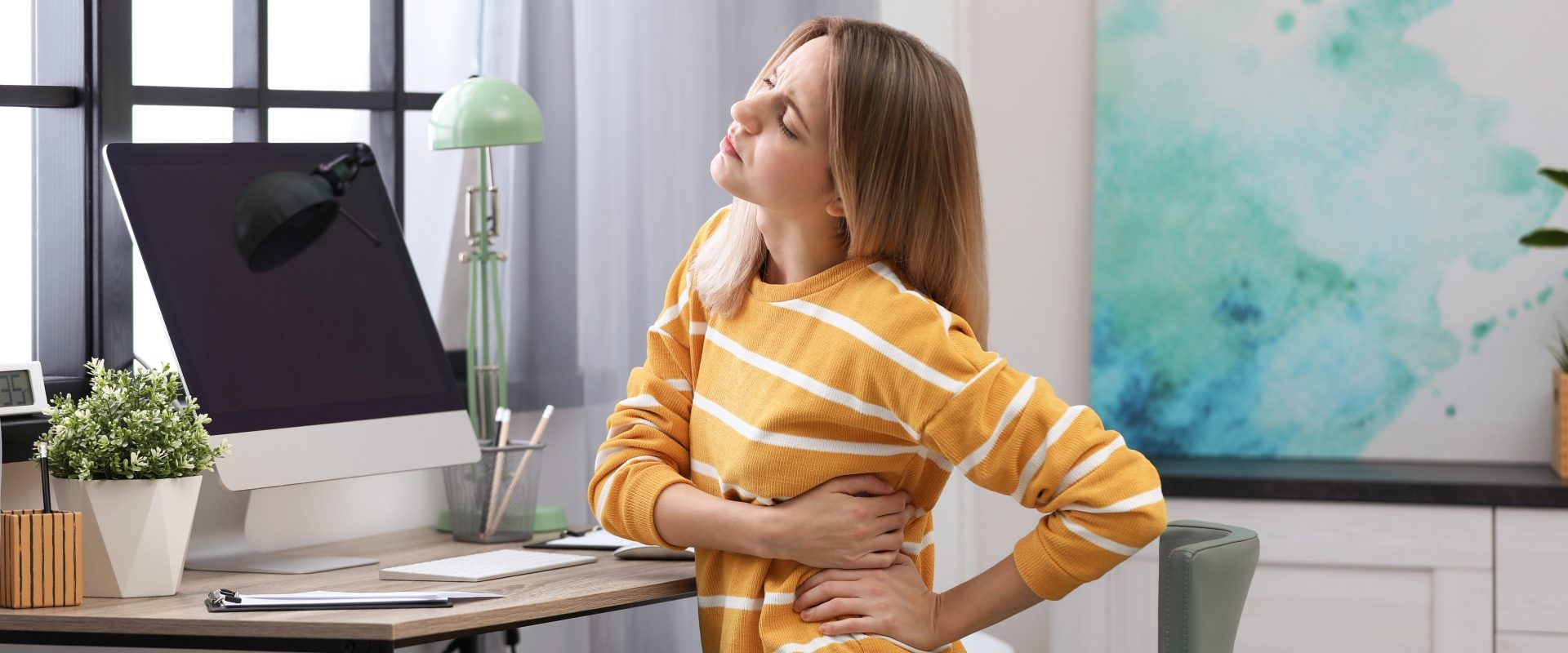 Choroby nerek - jakie dają objawy? Siedząca przy biurku kobieta cierpi z powodu bólu pleców.