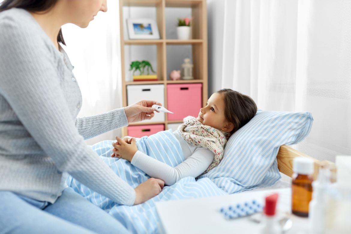 Choroby zakaźne wieku dziecięcego - jakie są objawy najczęstszych chorób u dzieci i jak je leczyć? Mama opiekuje się chorą córeczką, która leży w łóżku i mierzy jej temperaturę.