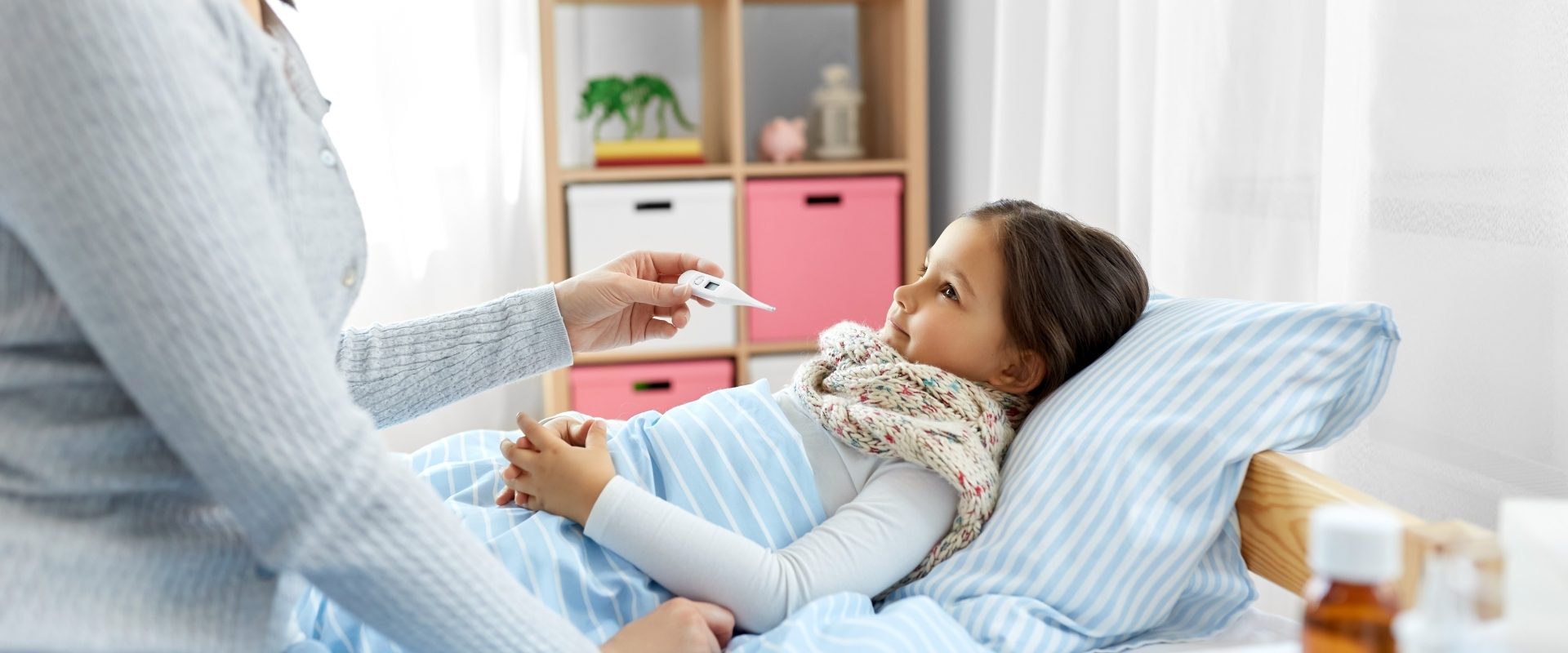 Choroby zakaźne wieku dziecięcego - jakie są objawy najczęstszych chorób u dzieci i jak je leczyć? Mama opiekuje się chorą córeczką, która leży w łóżku i mierzy jej temperaturę.