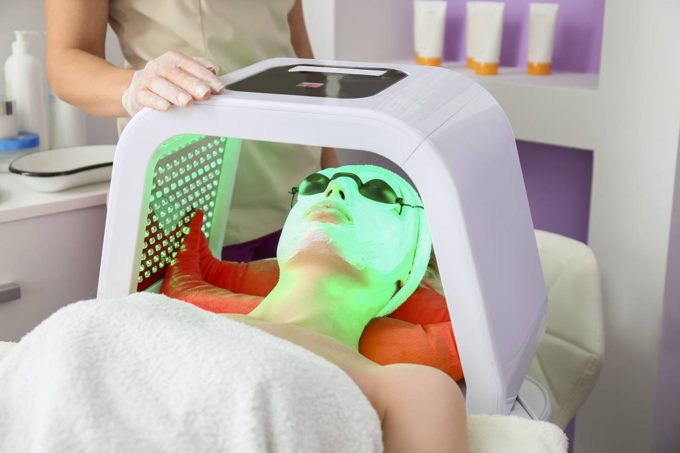 Na czym polega koloroterapia (chromoterapia)? Kobieta na zabiegu chromoterapii na twarz w gabinecie kosmetycznym (światło zielone).