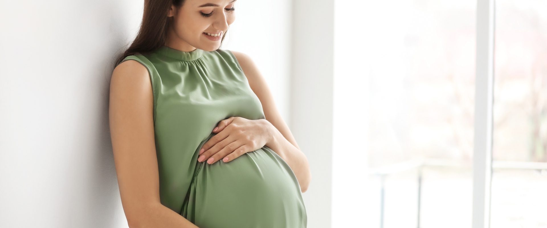 Ciśnienie w ciąży - jakie jest prawidłowe? Czym grozi nadciśnienie, a czym niedociśnienie? Kobieta w zaawansowanej ciąży w zielonej sukience dotyka swojego brzucha.