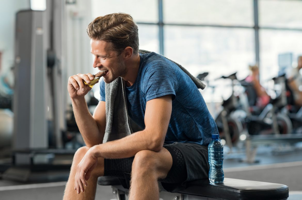5 najlepszych produktów żywieniowych dla mężczyzn: mięso, kapusta, jajka, brokuły i rzodkiewka. Mężczyzna je batona proteinowego po treningu na siłowni.