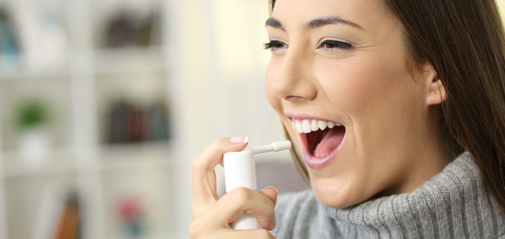 Co na gardło? Jak rozpoznać czy to wirusowe zapalenie gardła czy bakteryjne zapalenie gardła? Jakie zastosować leczenie? Jakie są sposoby na ból gardła wywołany przez wirusy, a jakie przez bakterie? Młoda atrakcyjna dziewczyna aplikuje spray do gardła.