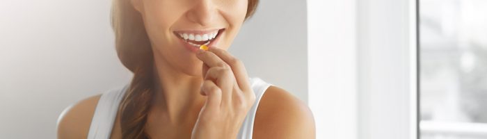 Czym jest efekt placebo i w jaki sposób nasz mózg pomaga organizmowi wrócić do zdrowia? Uśmiechnięta kobieta w białym topie połyka tabletkę, popijając ją szklanką wody.