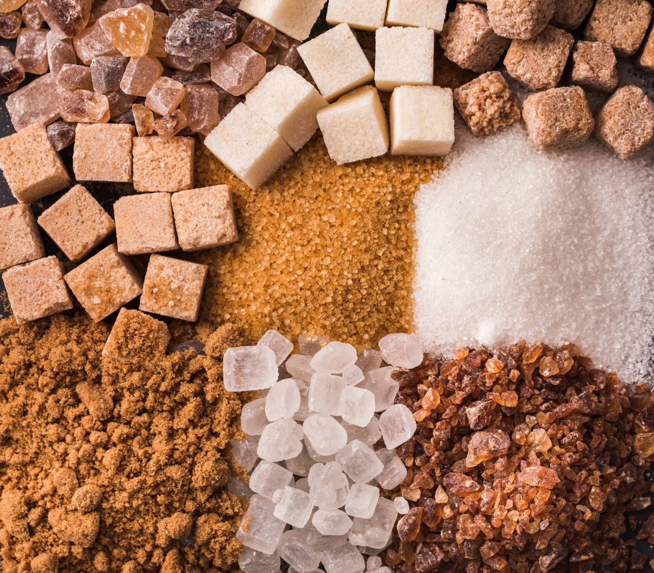 Cukier - słodka trucizna. Jak duża jest szkodliwość cukru? Różne rodzaje białego i brązowego cukru w kostkach, kryształkach i w postaci sypkiej ułożone obok siebie w kwadraty..