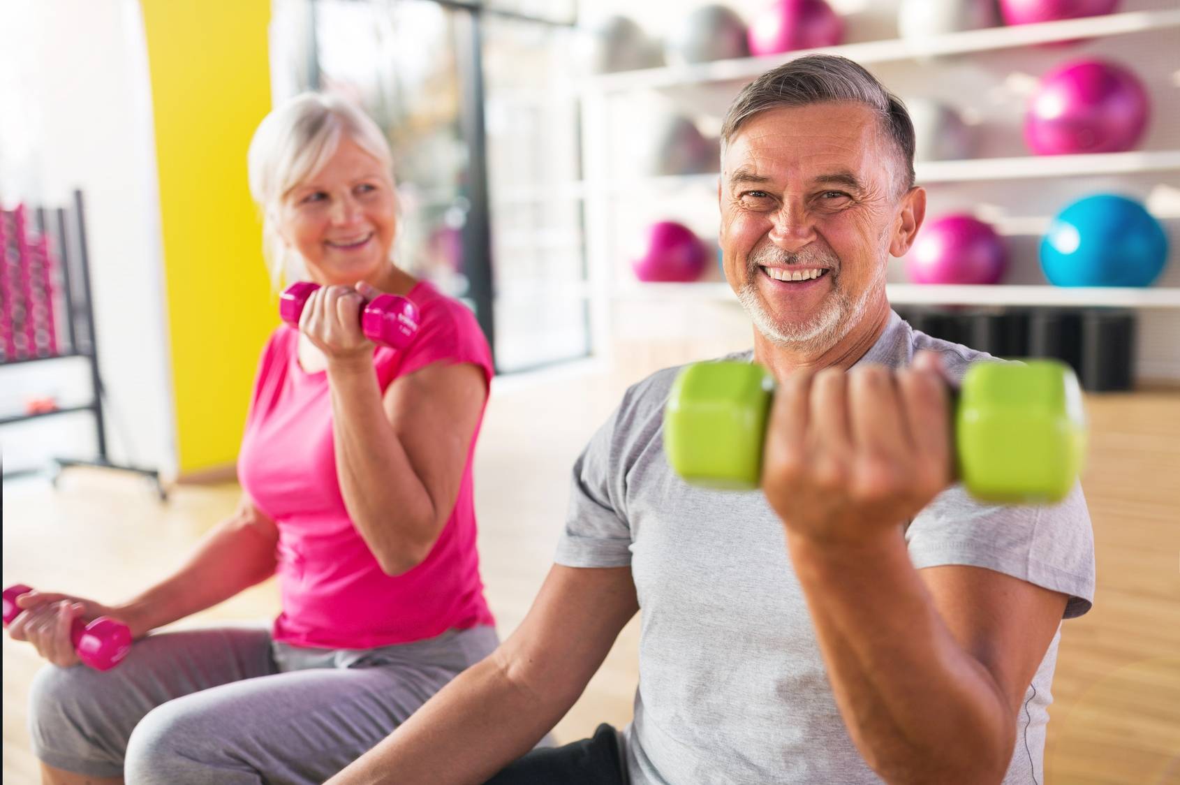Jakie ćwiczenia dla seniorów będą najlepsze i jak ćwiczyć na siłowni, aby zachować zdrowie? Starszy mężczyzna i kobieta ćwiczą z ciężarkami.
