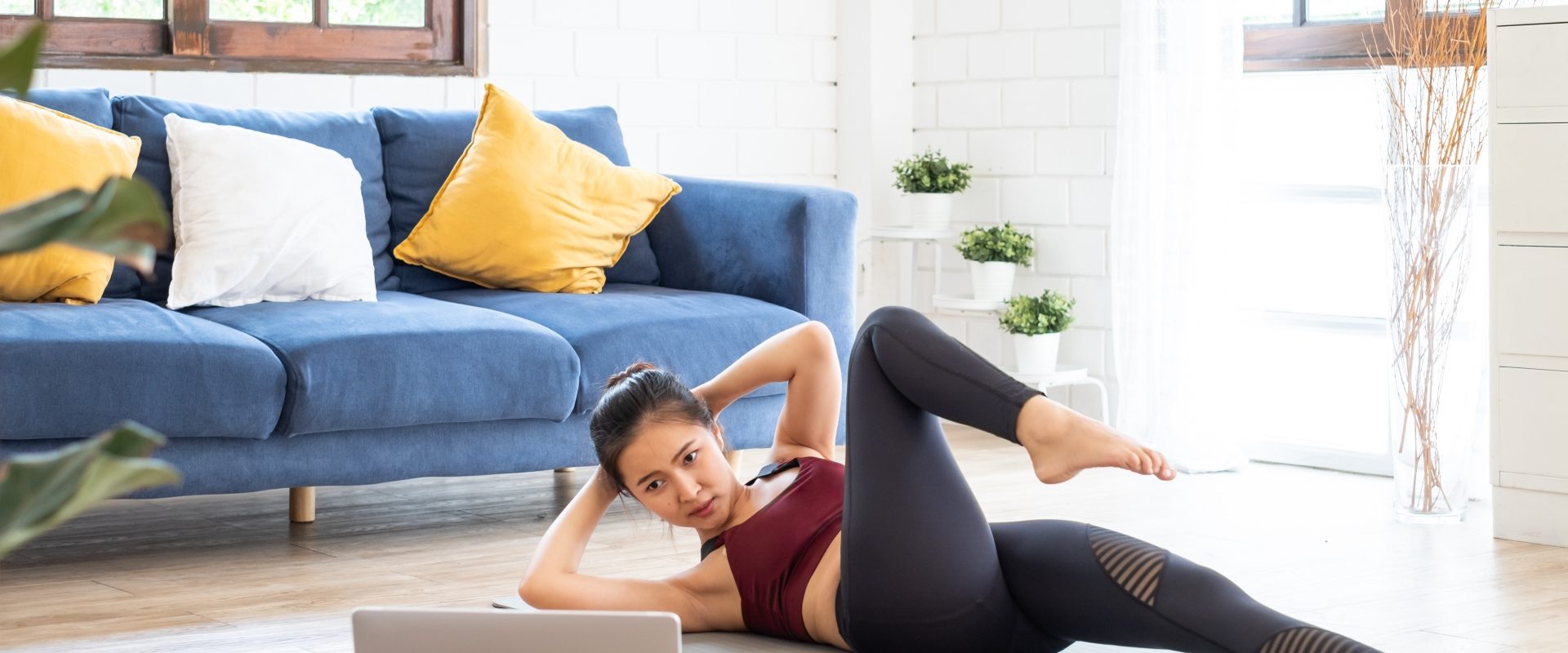 Ćwiczenia na kręgosłup piersiowy - jak je wykonać w domu? Kobieta ćwiczy na macie w salonie, patrząc w laptop, jak to robi trener online.