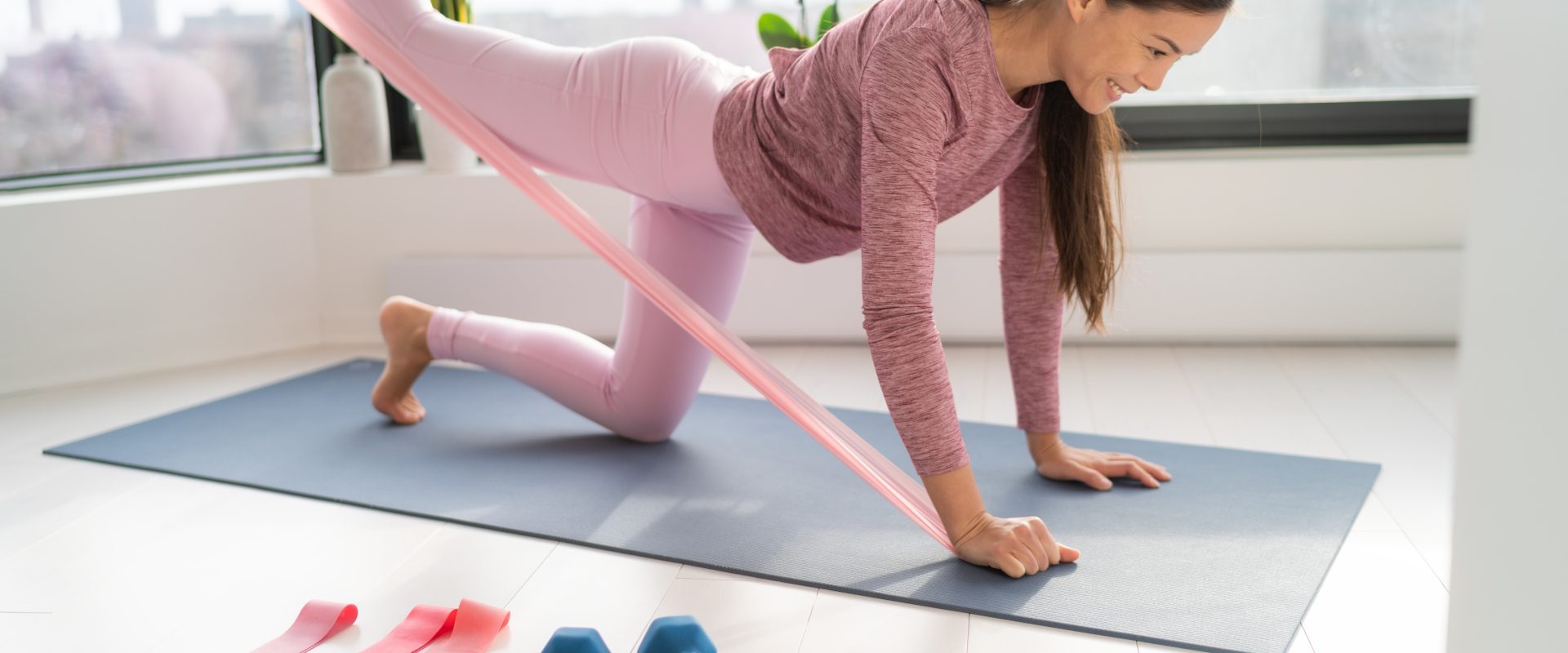 Kobieta wykonuje na macie ćwiczenia z gumą. Jak ćwiczyć z gumami w domu?