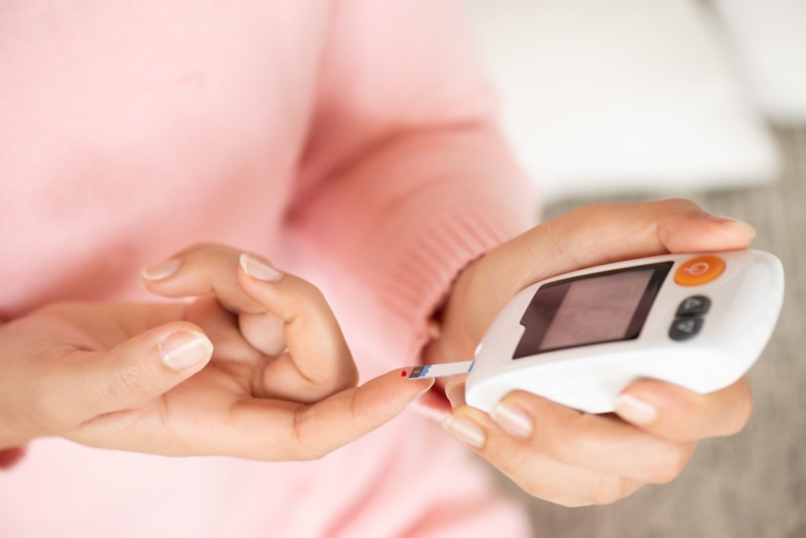 Cukrzyca typu 1 - objawy, przyczyny, leczenie. Jak radzić sobie i żyć z cukrzycą? Diabetyczka w różowym swetrze sprawdza poziom glukozy we krwi.