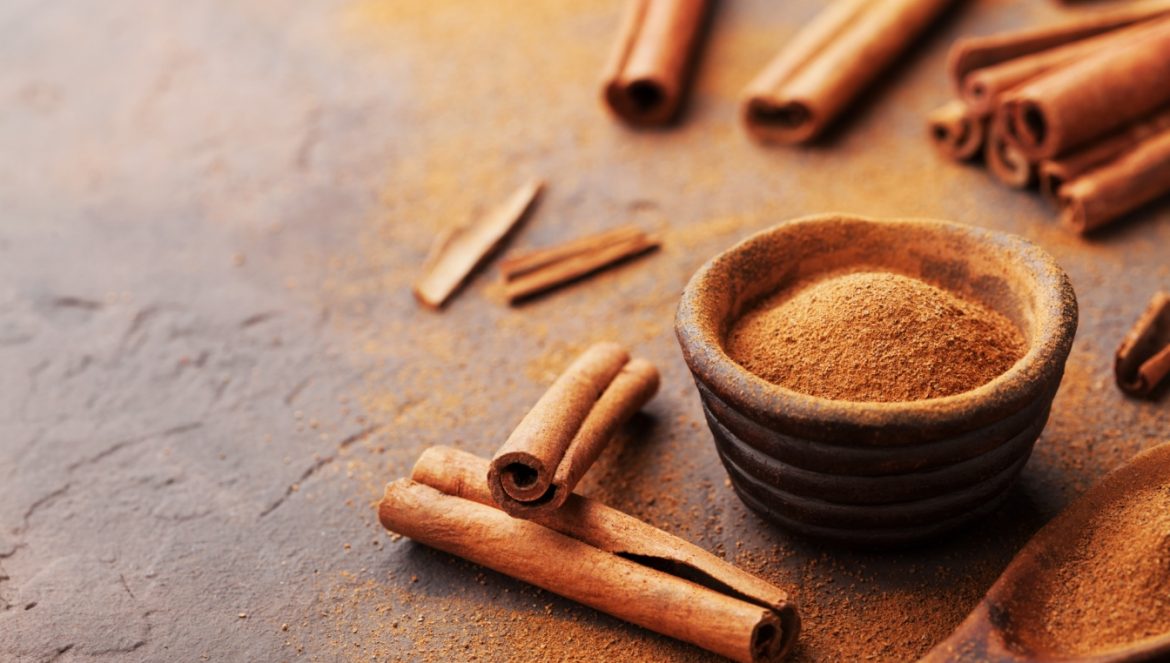 Cynamon - właściwości lecznicze i zastosowanie. Jak odróżnić cynamon cejloński od chińskiego? Laski cynamonu i sproszkowana kora w miseczce na ciemnym rustykalnym blacie.