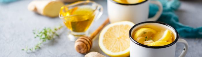 Dieta na odporność. Dwa białe kubki z herbatą z cytryną stoją na blacie, obok leży imbir, miód, cytryna.