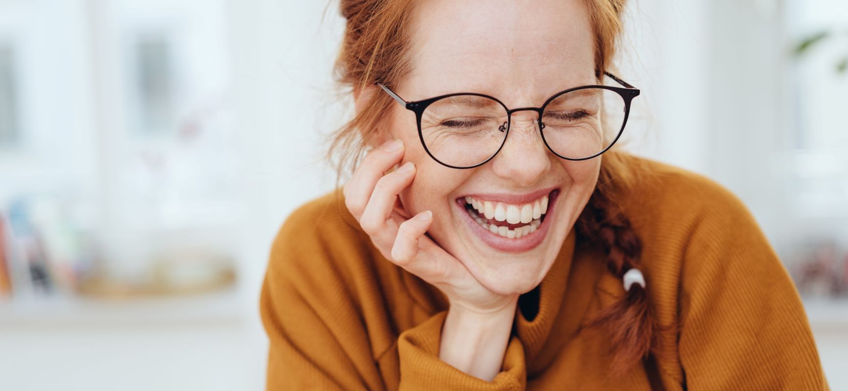 5 rzeczy, których potrzebują twoje oczy. Uśmiechnięta rudowłosa dziewczyna w musztardowym swetrze i okularach.