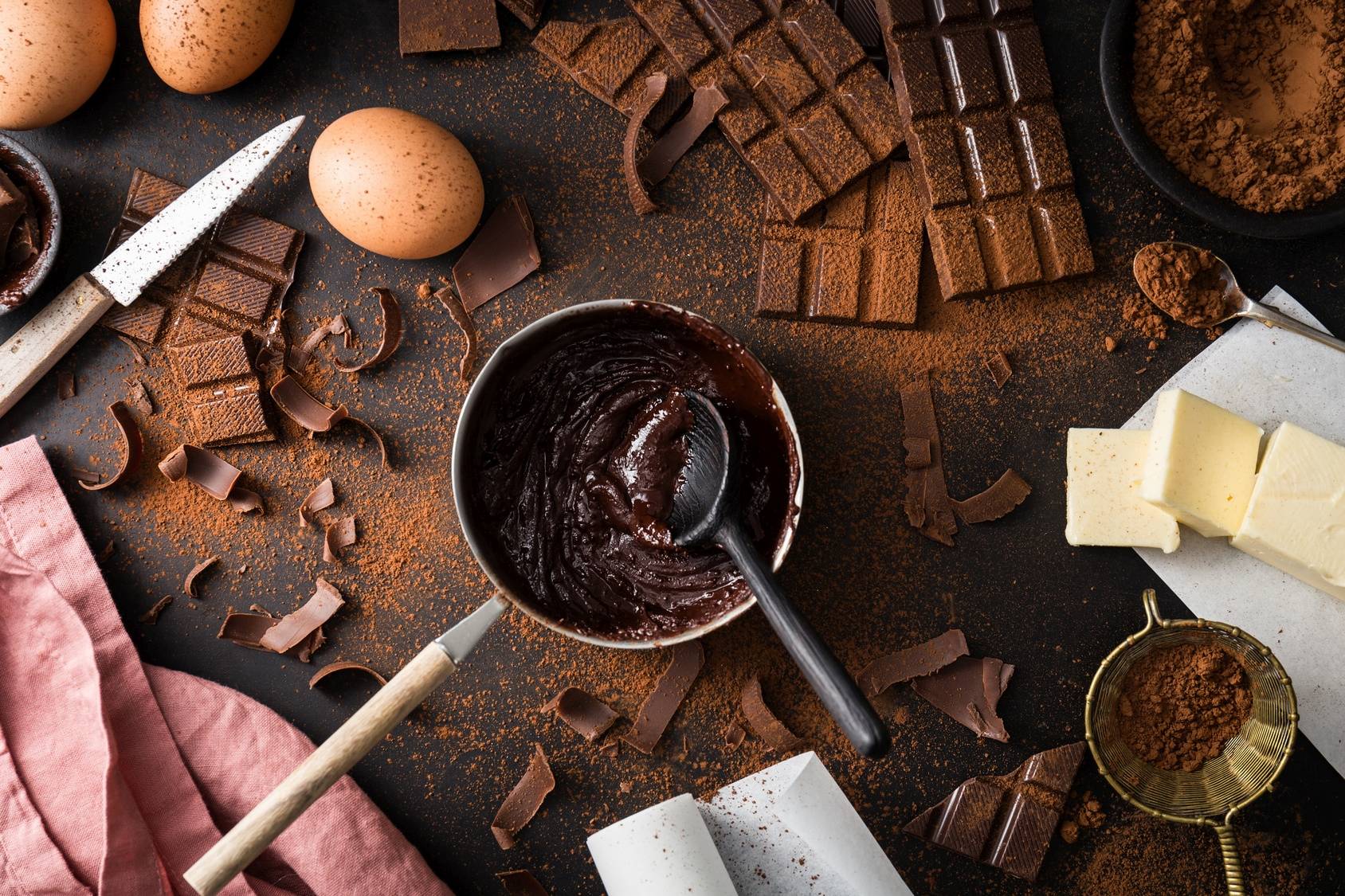 Produkcja gorzkiej czekolady. Kakao w garnuszku, wokół leżą tabliczki czekolady, jajka i masło.