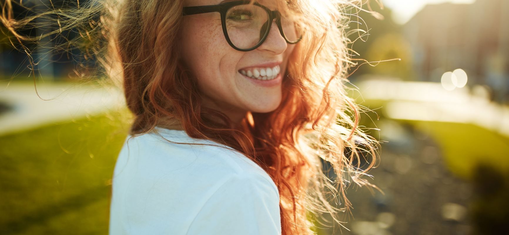 Czy optymizmu można się nauczyć? Uśmiechnięta rudowłosa dziewczyna w okularach z czarnymi rogowymi oprawkami uśmiecha się do obiektywu.