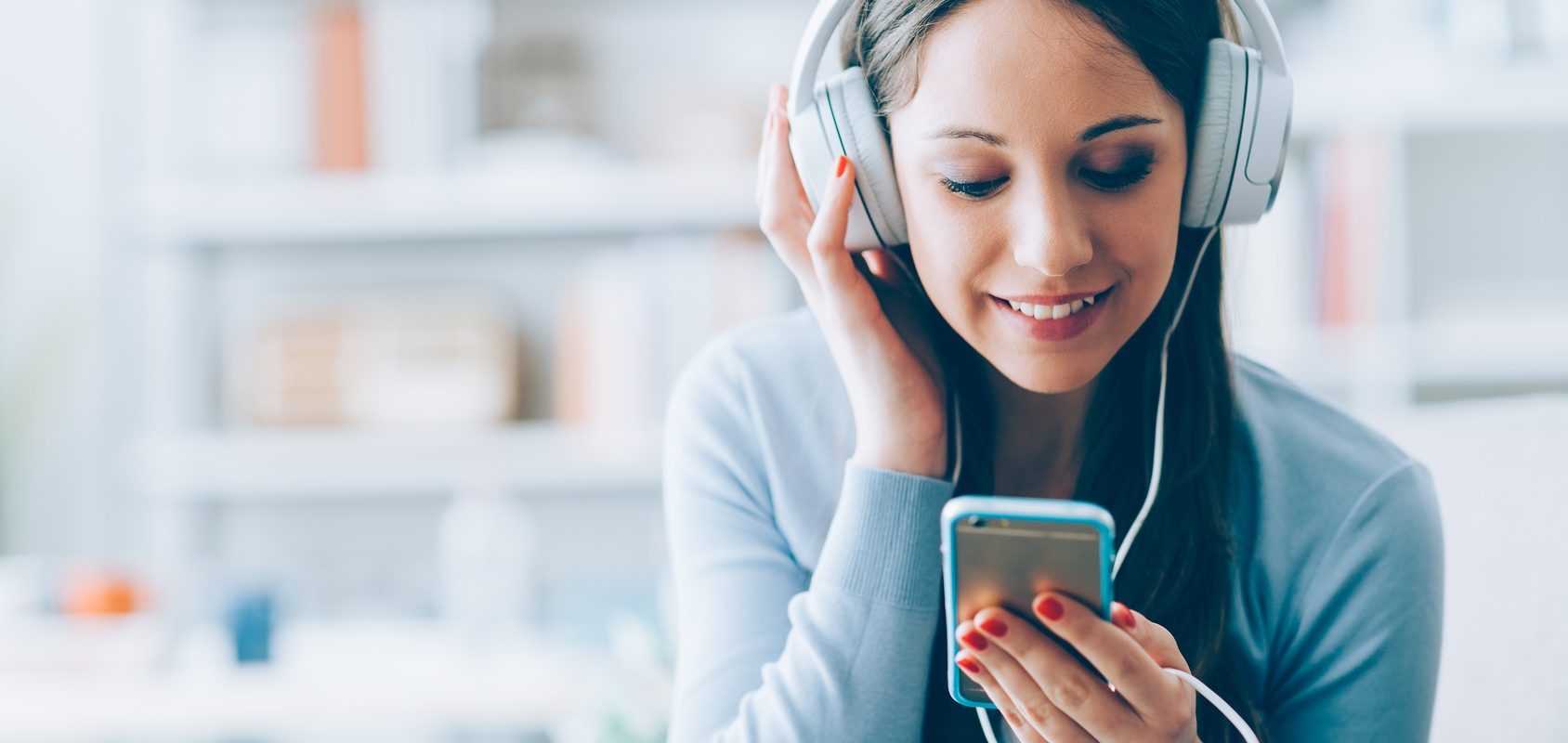Czy smartfony powodują zawroty głowy? Młoda dziewczyna słucha muzyki ze smartfonu na słuchawkach nausznych.