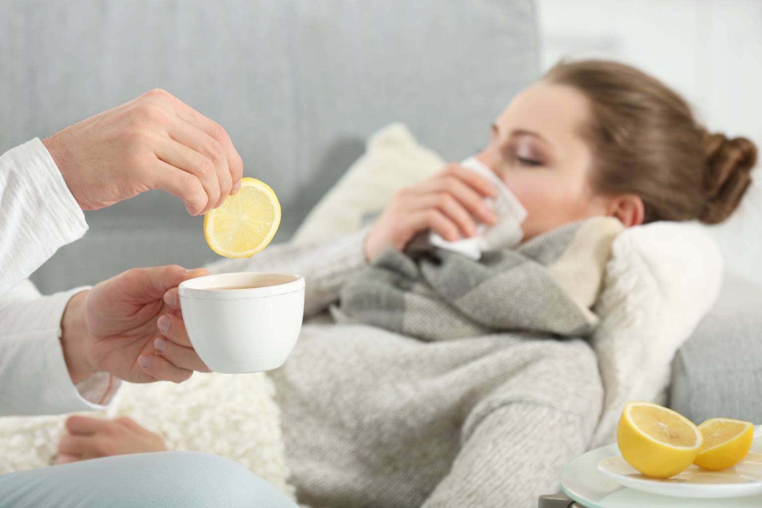 Przeziębienie a witamina C - dlaczego w medycynie chińskiej nie dodaje się cytryny do herbaty podczas infekcji? Przeziębiona kobieta leży na kanapie w salonie, a obok siedzi opiekun, podający jej herbatę z cytryną.