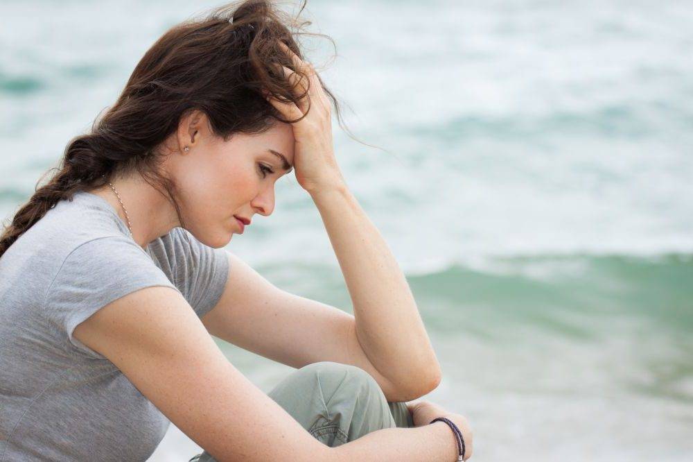 Trauma - jak sobie z nią radzić? Smutna, załamana kobieta siedzi nad brzegiem morza i się zamartwia.