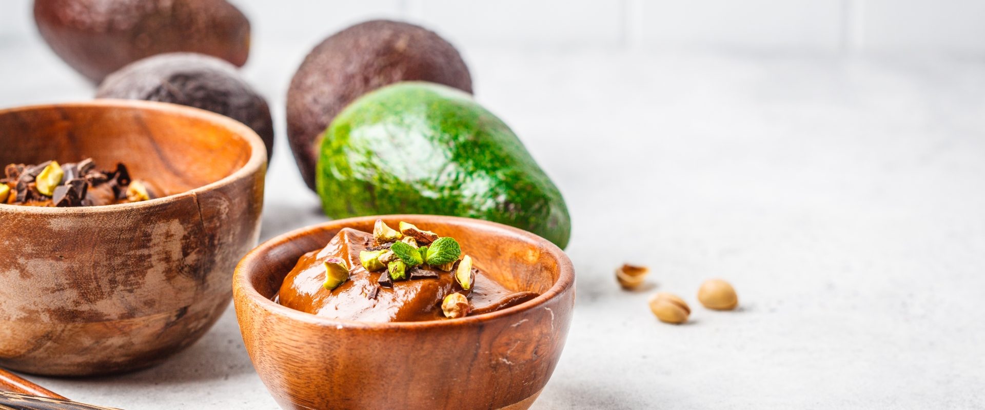 Przepisy na awokado na słodko. Budyń czekoladowy z awokado w drewnianej miseczce na białym blacie.