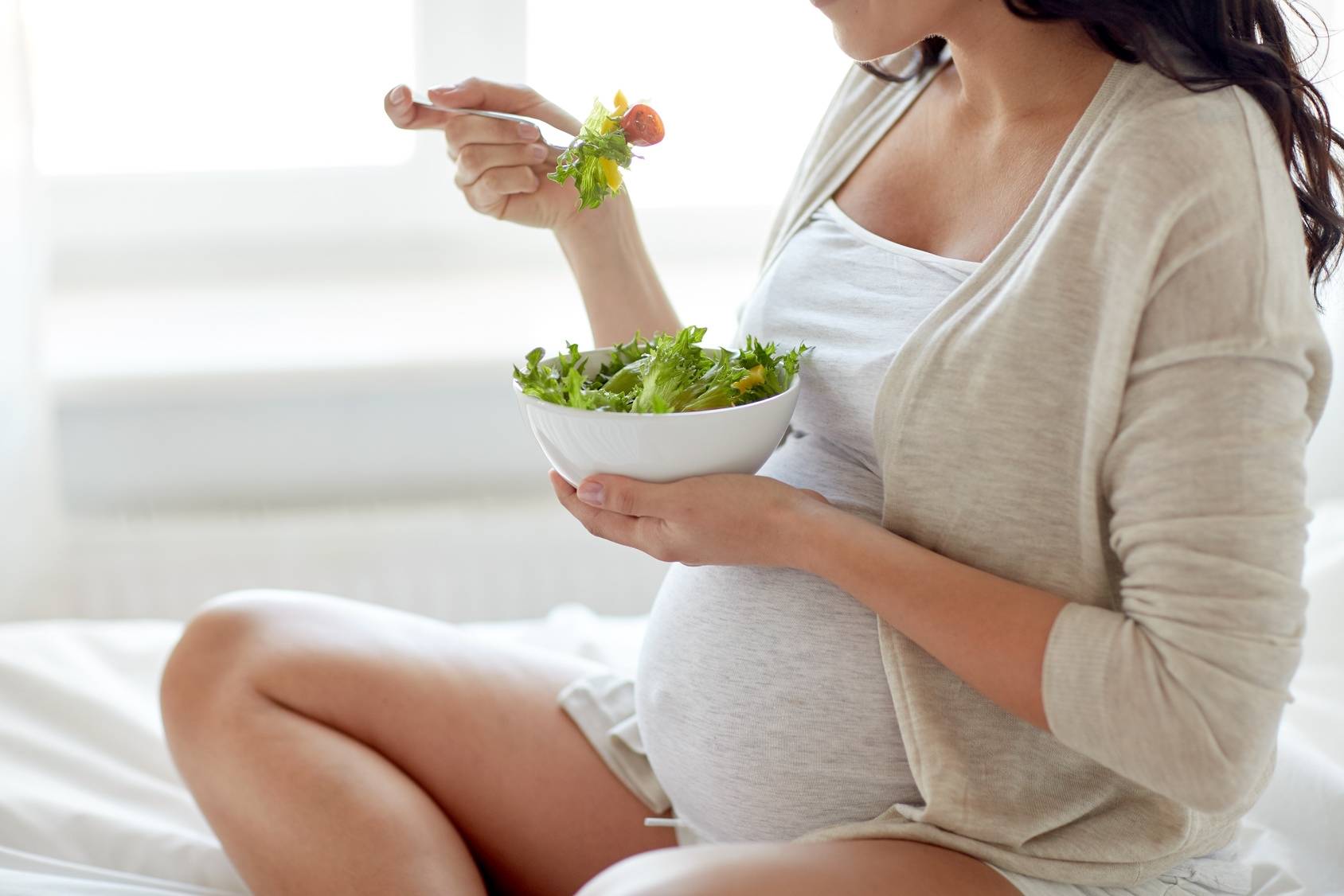 Suplementy w ciąży - jak zadbać o prawidłowy rozwój dziecka? Zbliżenie na ciężarną kobietę jedzącą sałatkę.