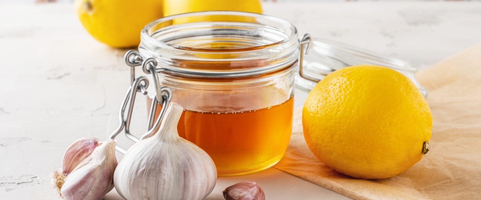 Domowe syropy na odporność i infekcje. Słoik miodu, czosnek i cytryny leżą na blacie kuchennym.