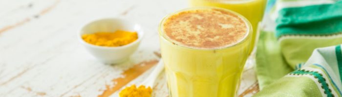 Złote mleko - przepis lek na przeziębienie i grypę. Dwie szklanki z żółtym mlekiem z kurkumą.