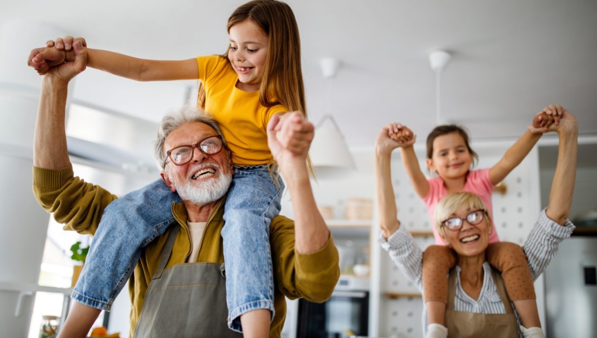 Jak skrypty pokoleniowe wpływają na nasze życie? Babcia i dziadek bawią się z wnukami nosząc ich na barana po domowym salonie.