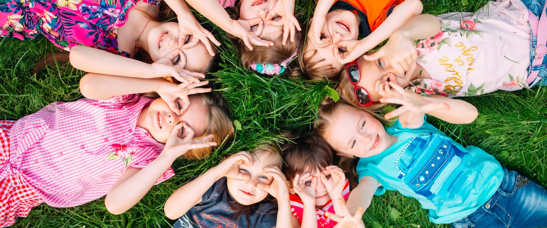 Mononukleoza zakaźna - jakie są jej objawy, przyczyny i jak ją leczyć. Grupa dzieci leżących na trawie w kółeczku i przykładających dłonie do oczu na kształt lornetki.