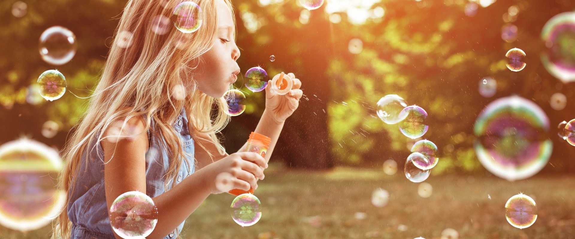 Astma u dzieci - jak rozpoznać objawy i jak leczyć? Blondwłosa dziewczynka puszcza bańki mydlane w letniej sielankowej scenerii.
