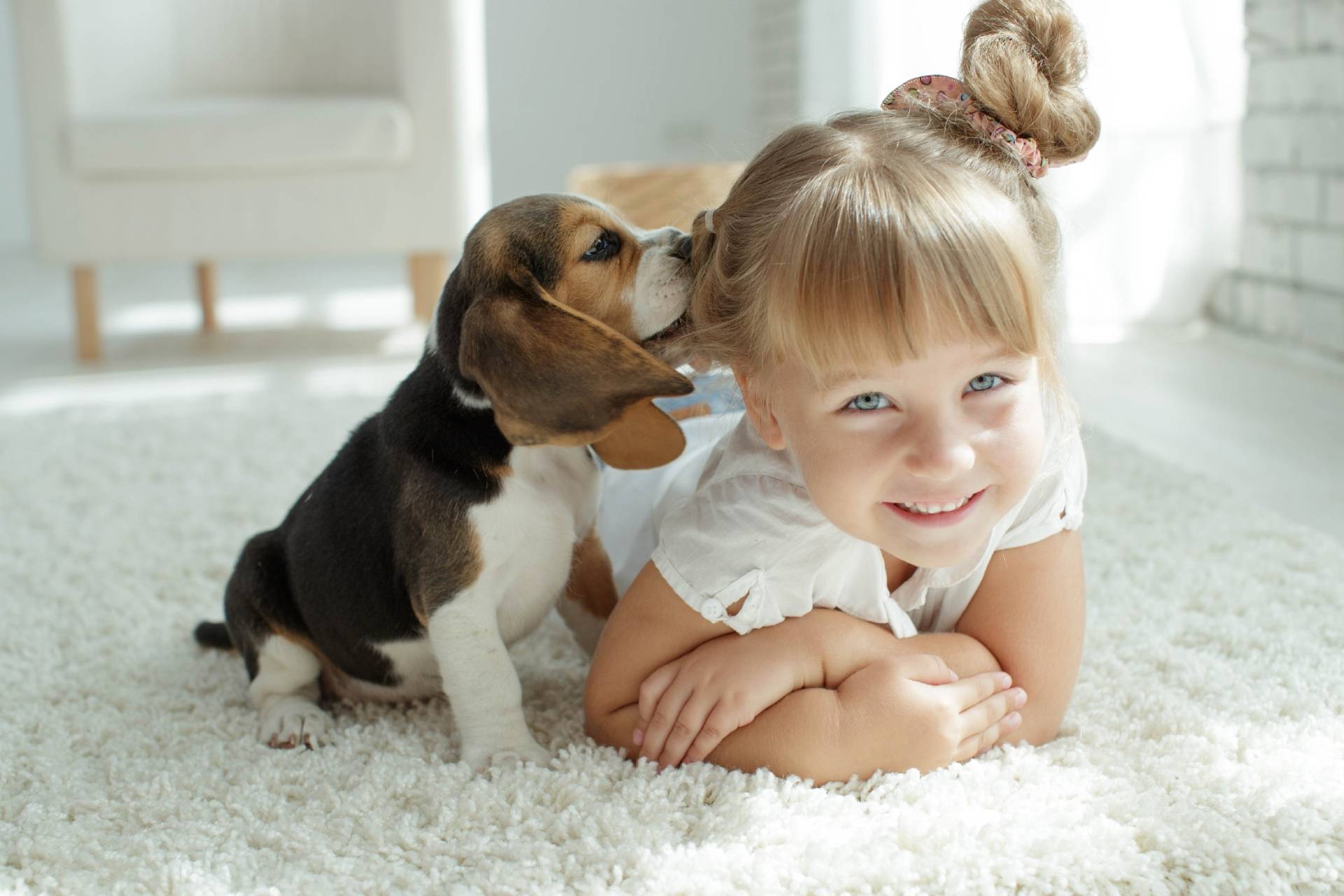 Leki homeopatyczne dla zwierząt. Mała dziewczynka leży na dywanie ze szczeniakiem.