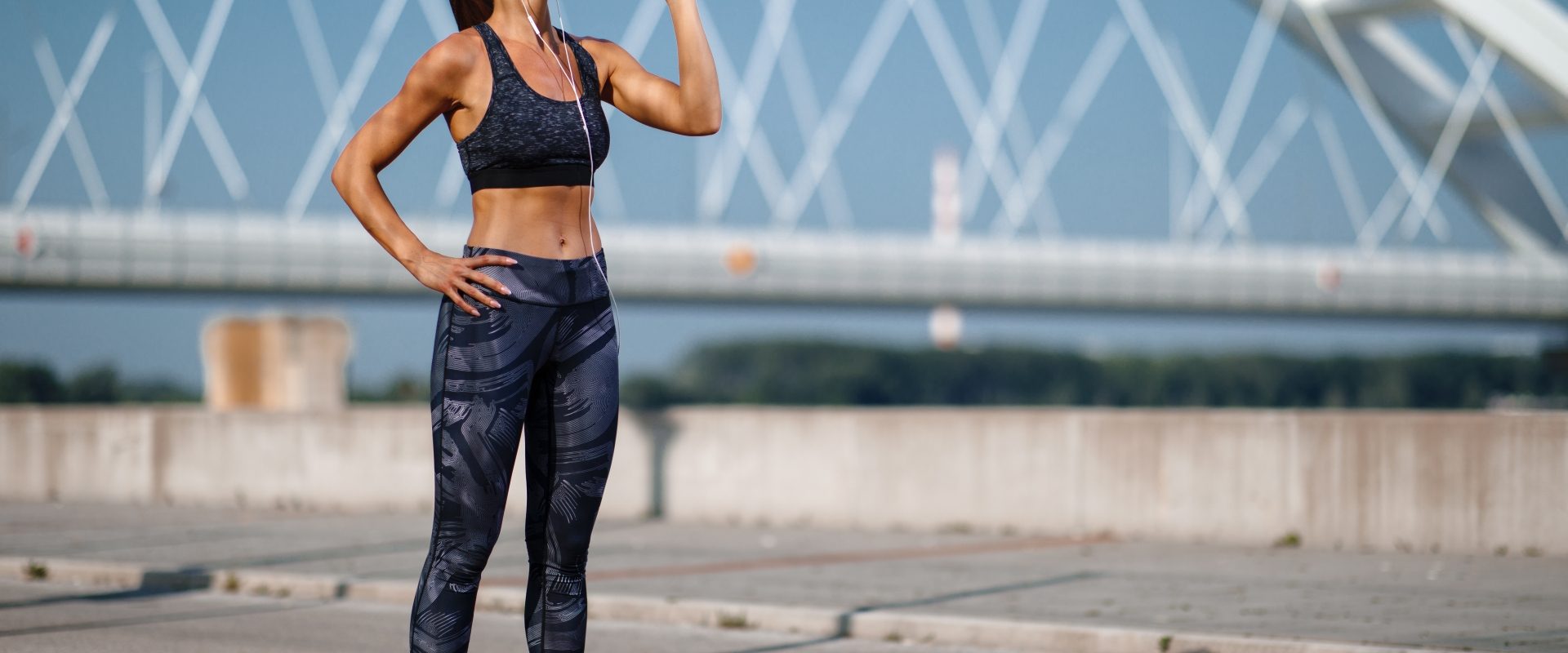 Elektrolity - czym są, jaką pełnią funkcję w organizmie, jakie są przyczyny i objawy niedoboru elektrolitów? Wysportowana kobieta pije napój izotoniczny z bidonu po treningu biegania po mieście.