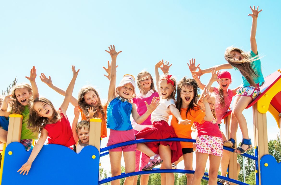 Elektrolity dla dzieci - kiedy je stosować? Grupa kolorowo ubranych szczęśliwych dzieci stoi na mostku.