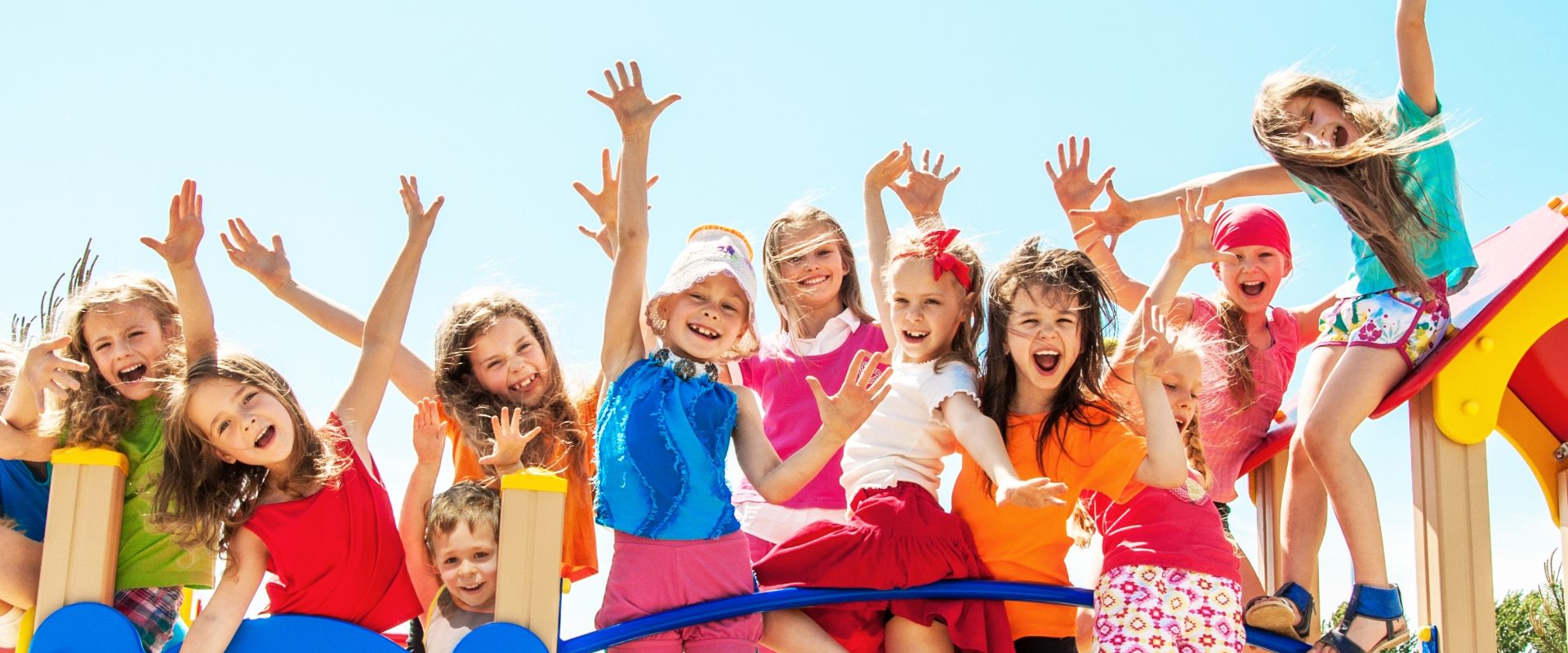 Elektrolity dla dzieci - kiedy je stosować? Grupa kolorowo ubranych szczęśliwych dzieci stoi na mostku.